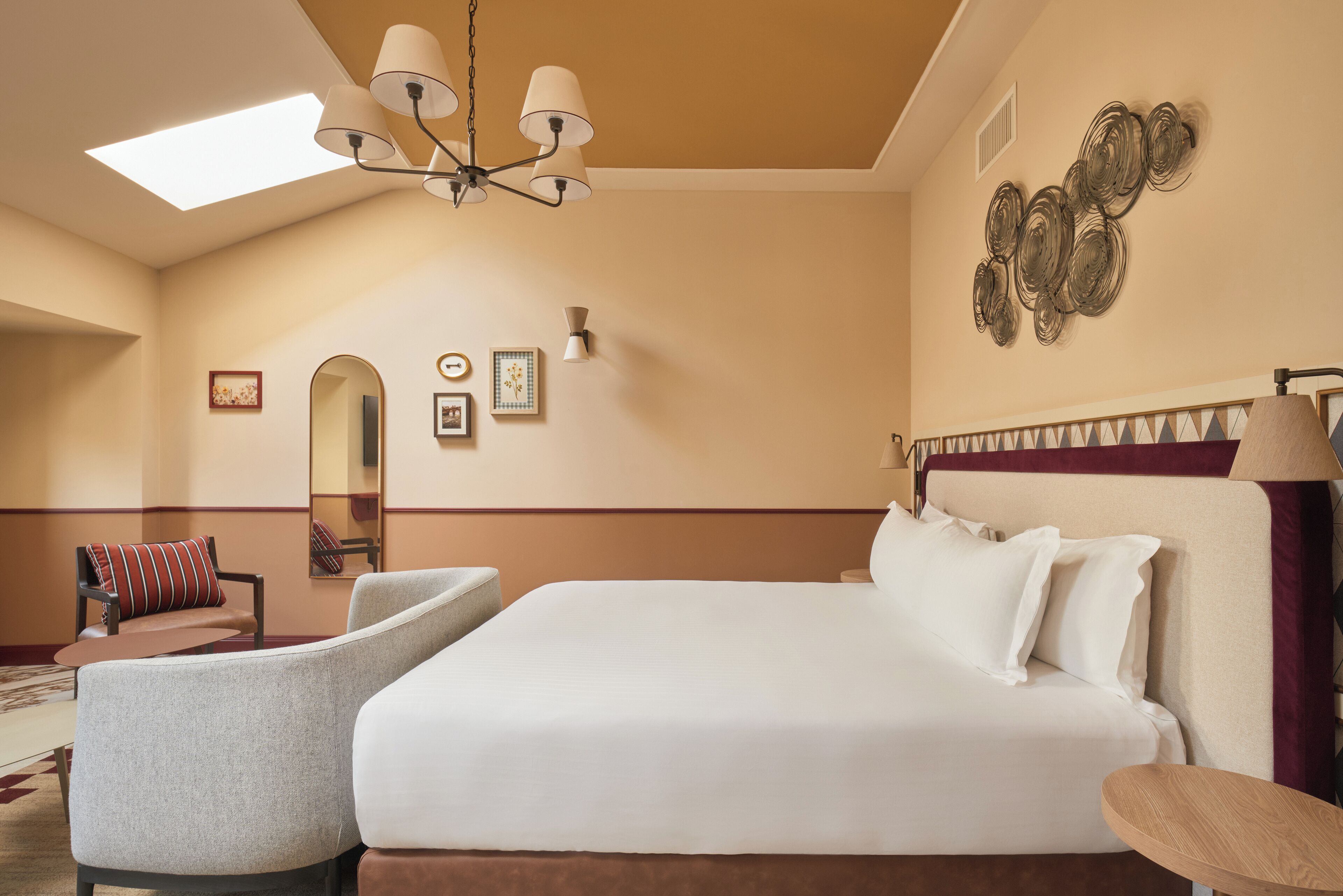 Habitación de hotel con una cama grande, una silla, un escritorio y una araña.