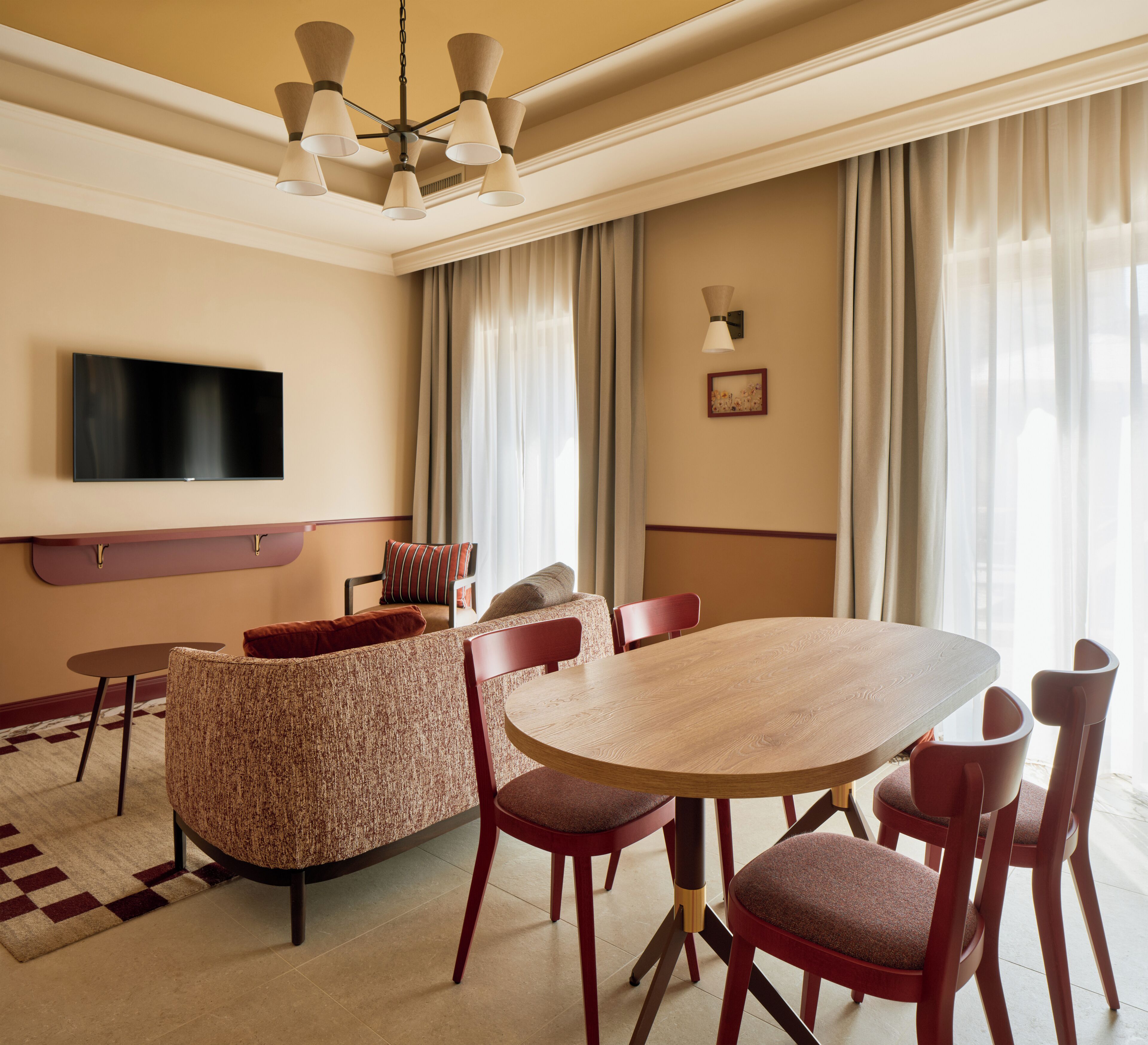 A hotel room with a flat-screen TV, a dining table with chairs, a sofa, and a chandelier.