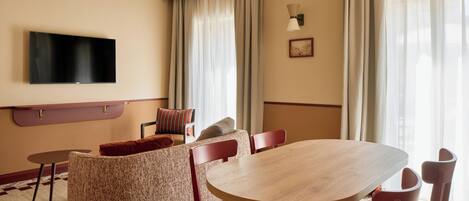 A hotel room with a flat-screen TV, a dining table with chairs, a sofa, and a chandelier.