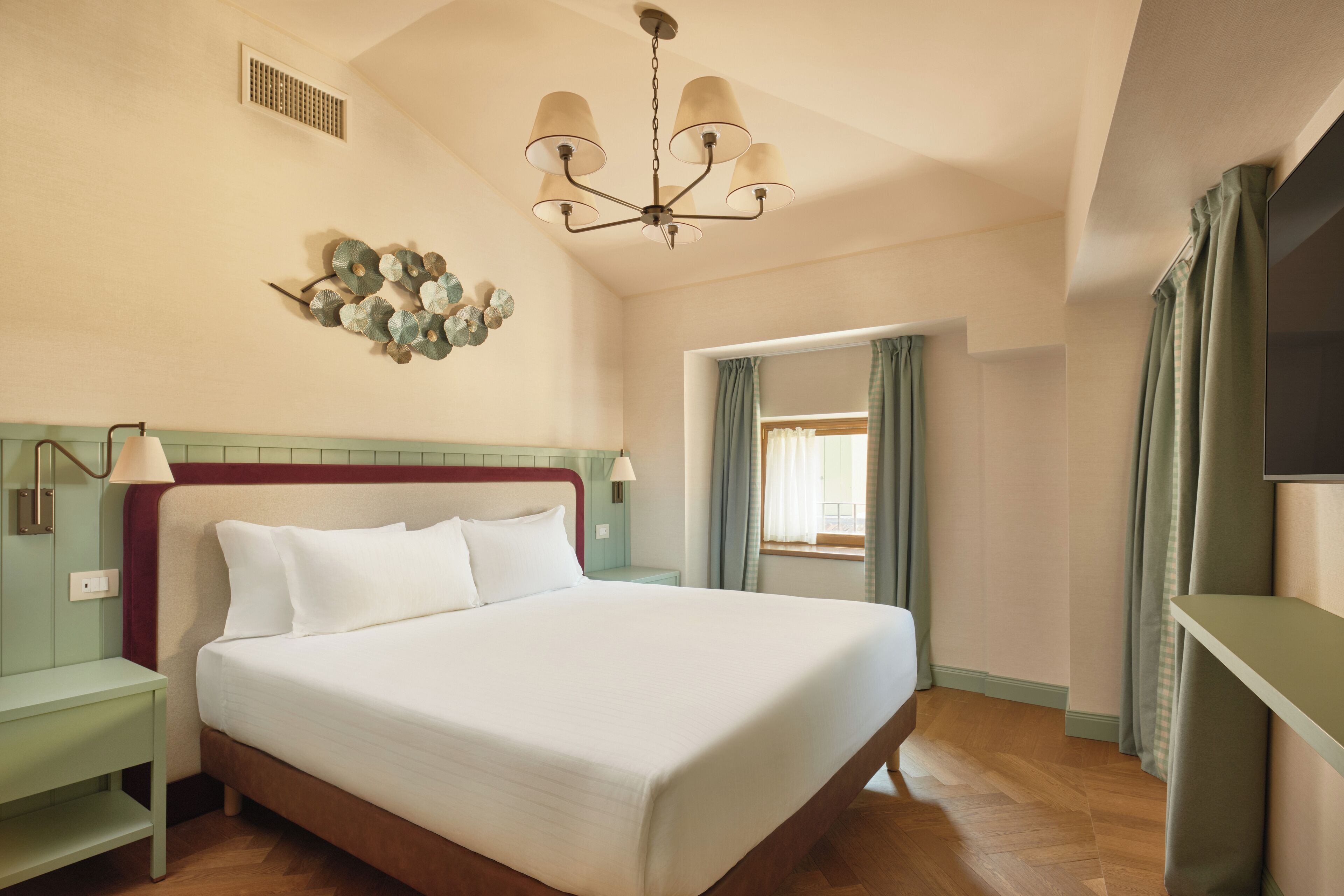 A neatly arranged hotel room with a large bed, a bedside table, a wall-mounted lamp, and a ceiling light fixture.