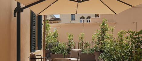 An outdoor patio with a table and chairs, a large umbrella, and potted plants.