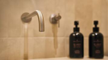 A bathroom sink with a chrome faucet, two black soap dispensers, and a tiled wall.