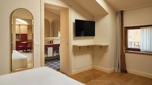 Ein Schlafzimmer mit Oberlicht, einem an der Wand montierten Fernseher, einem Bett, einem Spiegel und einem durch eine offene Tür einsehbaren Badezimmer.