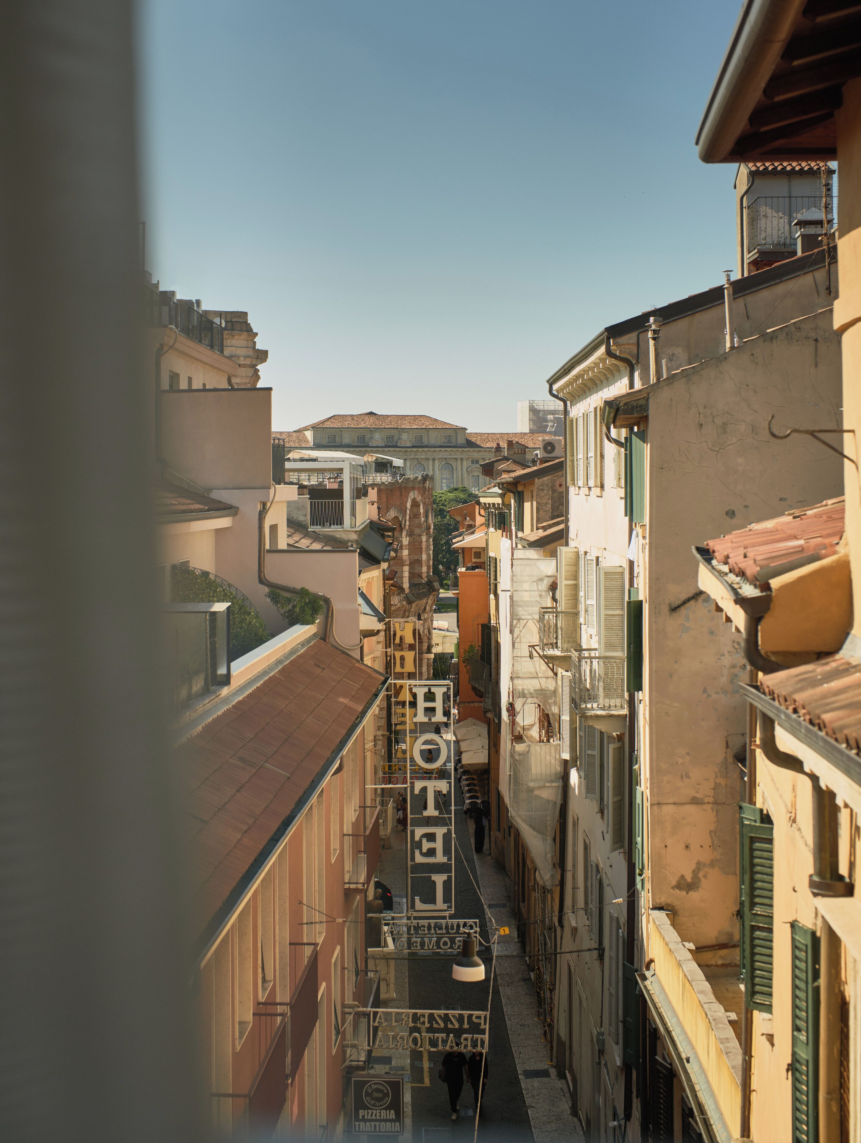 A narrow street with buildings on either side, a clear sky, and a distant view of a large building with a dome.