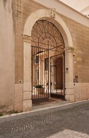 Una entrada en arco con una reja de hierro forjado, un muro de piedra y una calle adoquinada.