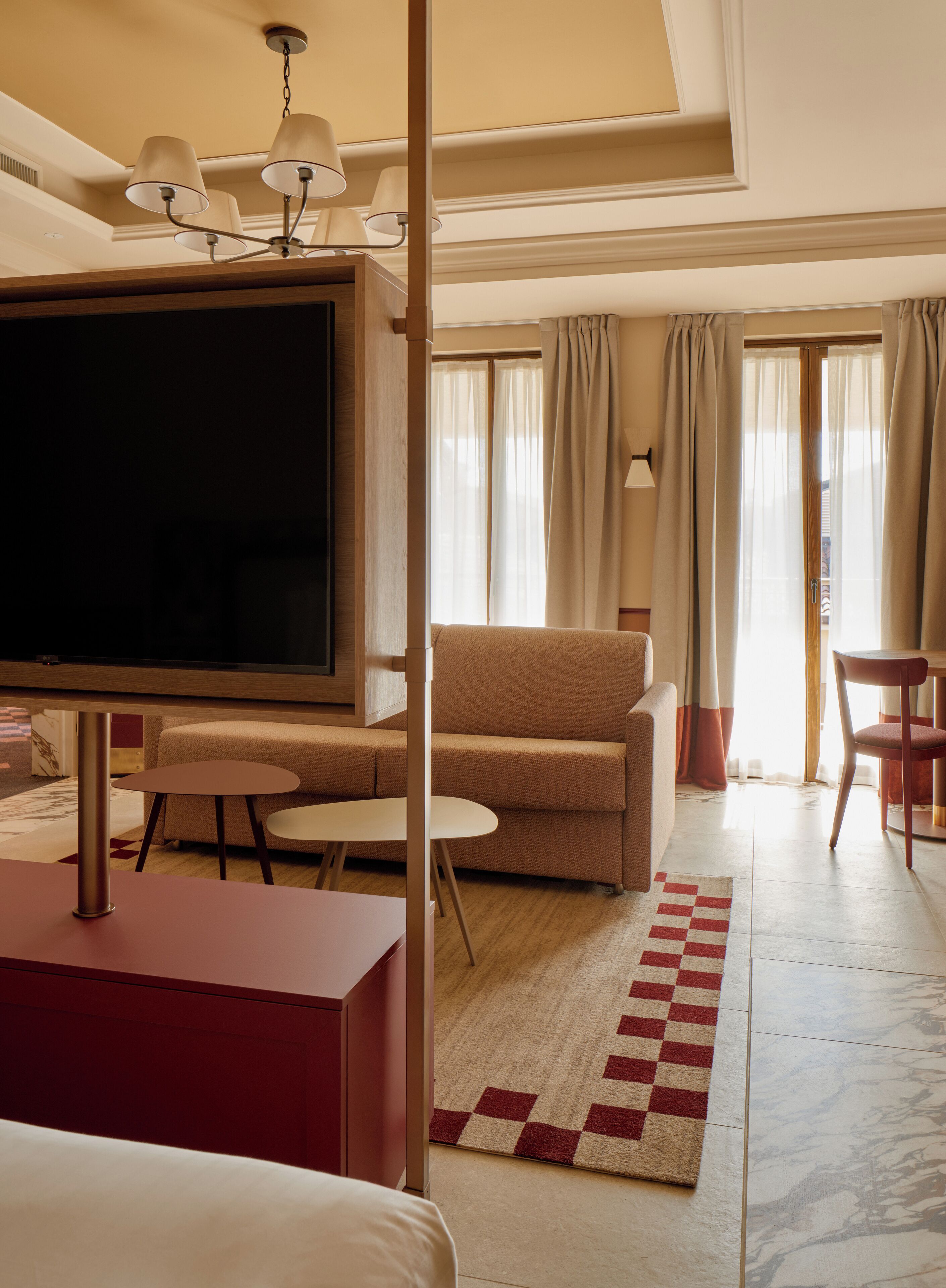 Ein Hotelzimmer mit Fernseher, einer Couch, einem Sessel, einem kleinen Tisch und einem karierten Teppich.
