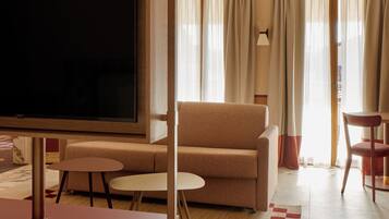A hotel room with a TV, a sofa, a chair, a small table, and a checkered rug.