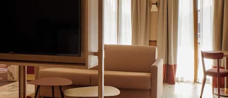 Habitación de hotel con televisión, sofá, sillón, una mesita y alfombra a cuadros.