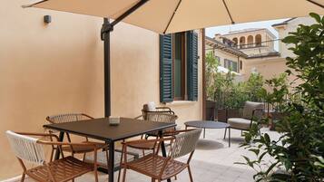 An outdoor patio with a table and chairs, a large umbrella, and a view of a building with balconies.
