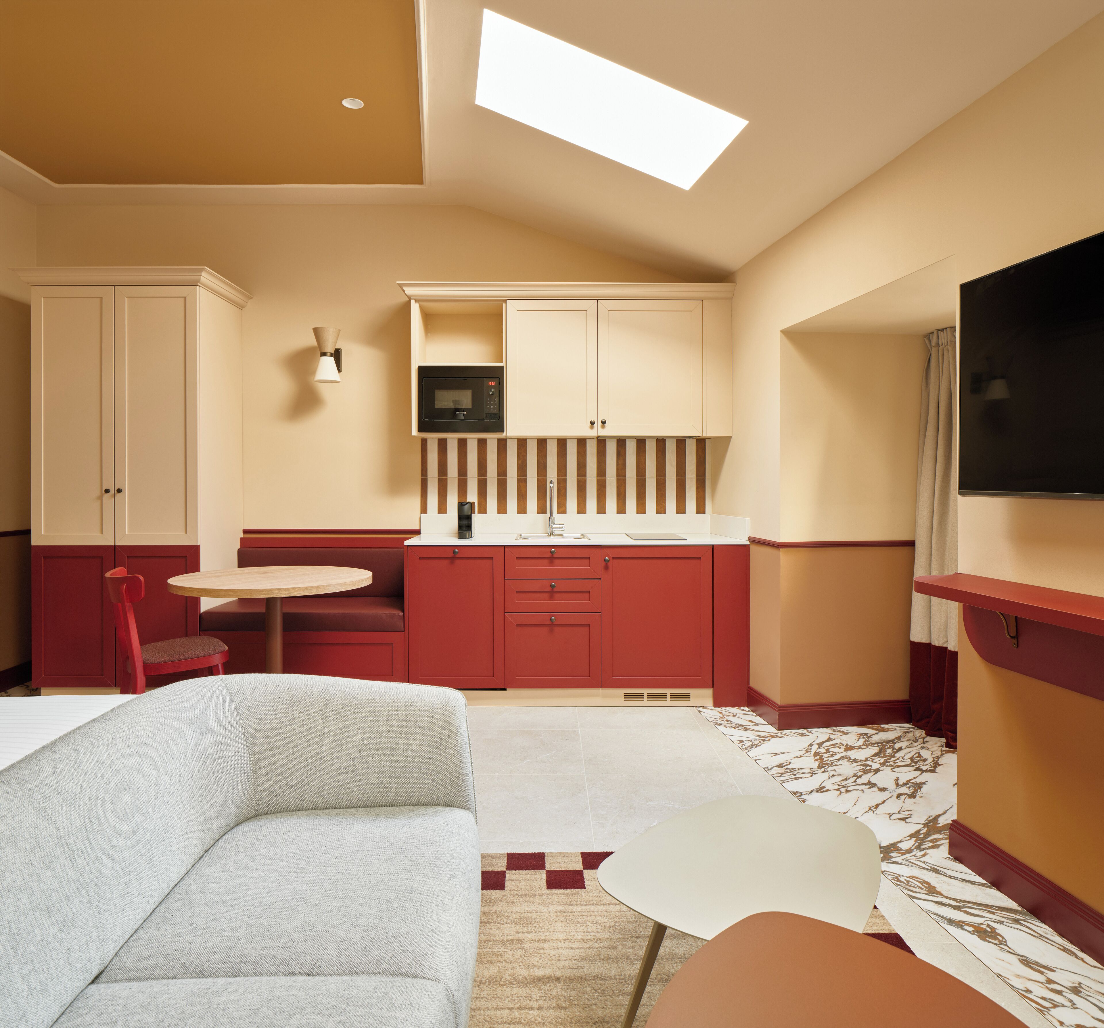 A compact kitchen with a microwave, a small dining table, and a red chair.