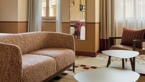 A hotel room with a sofa, two small tables, a mirror, and a view of the outside through large windows. - Homy Livia Verona (Verona)