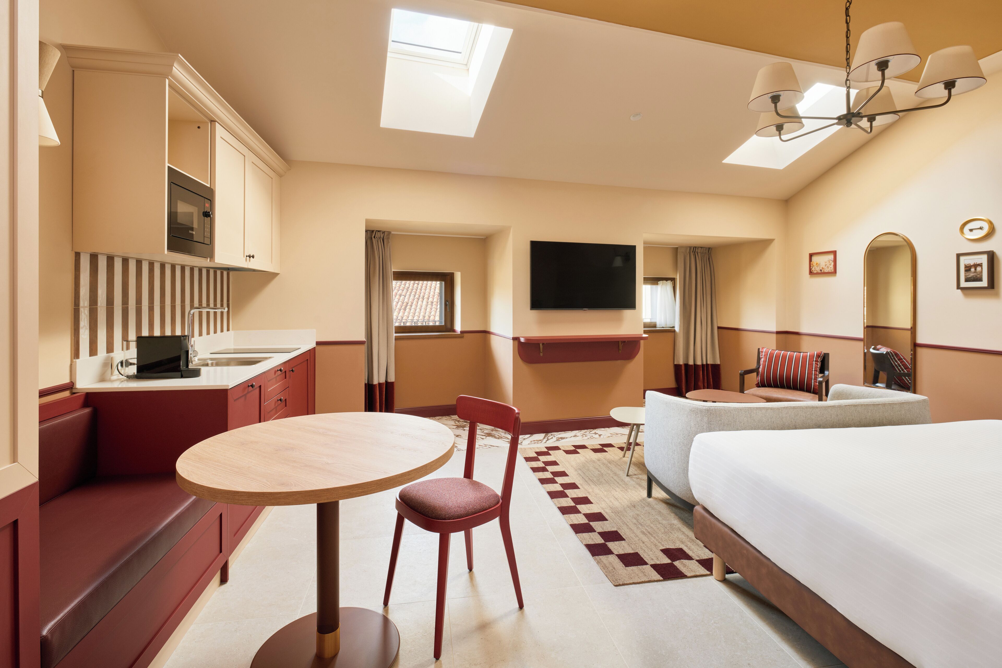 A hotel room with a bed, a dining table, a chair, a TV, and a kitchenette.