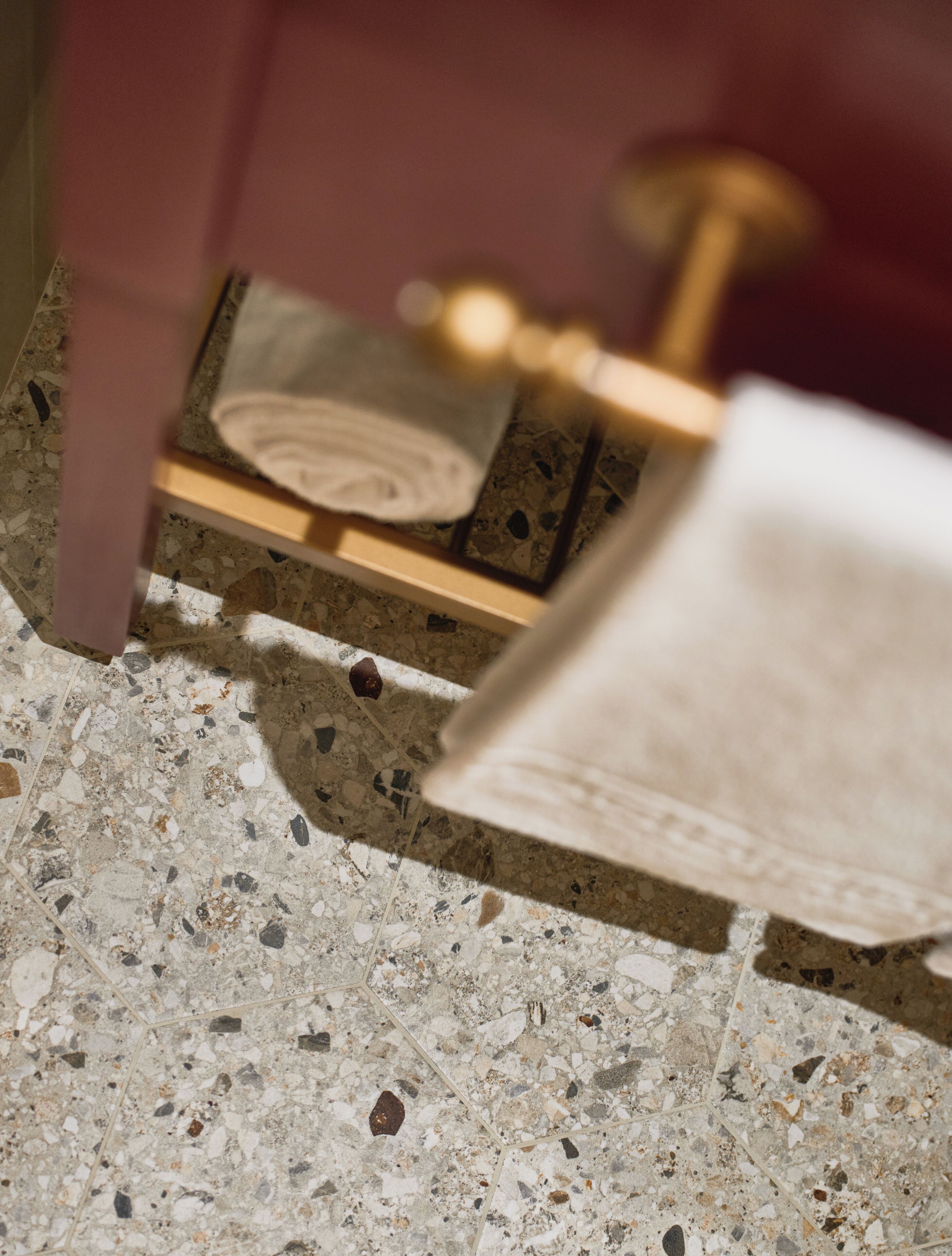 A close-up of a terrazzo floor with a geometric pattern, a wooden chair, and a brass object that appears to be a part of a piece of furniture.