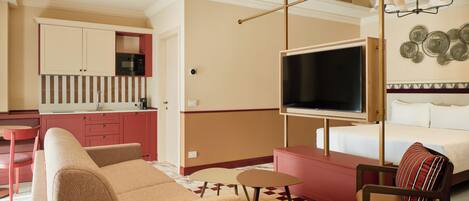 A modern hotel room with a sofa, a chair, a TV, and a kitchenette.