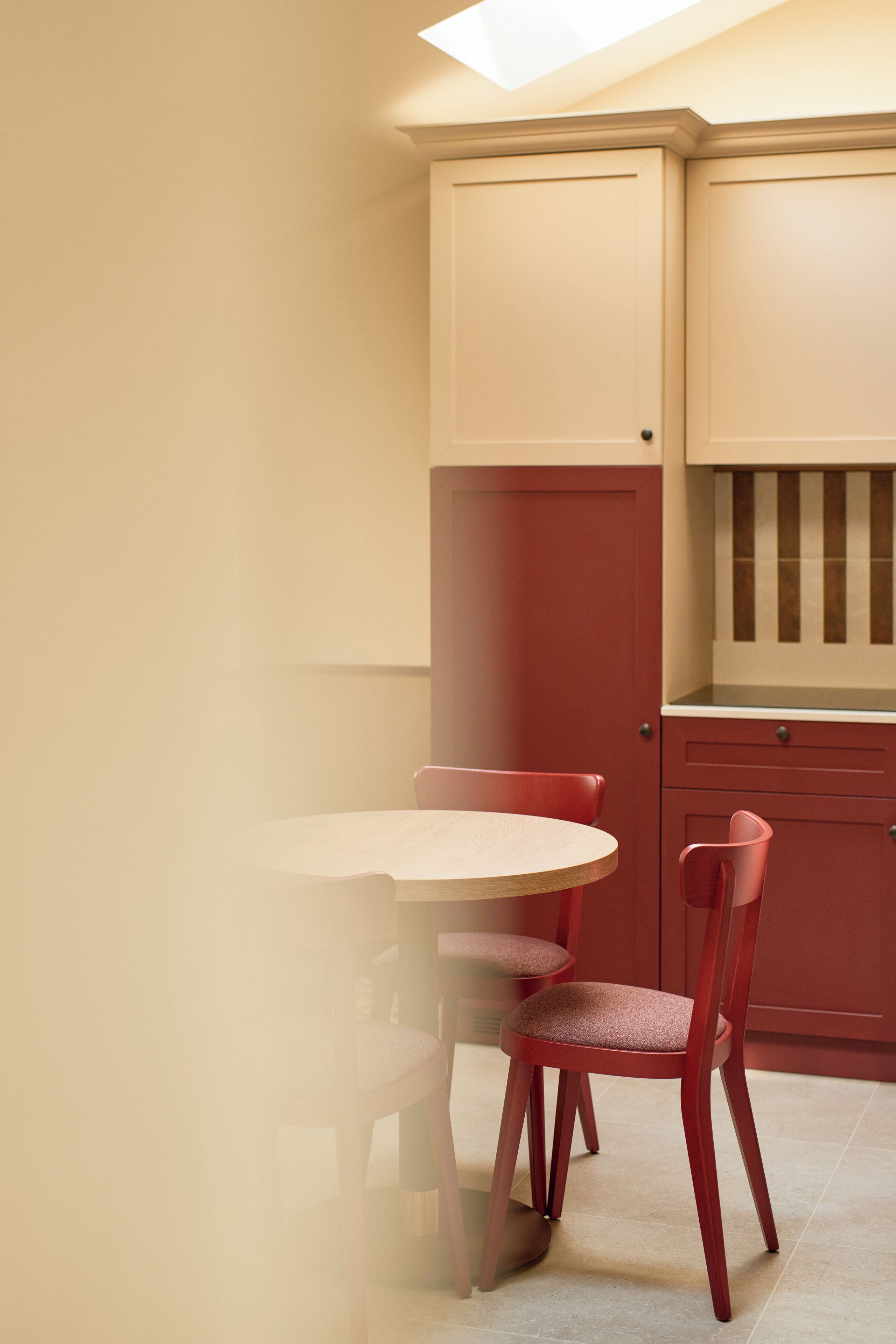 Une cuisine avec une table ronde et deux chaises rouges, des placards de couleur beige et une fenêtre au-dessus de l’évier.