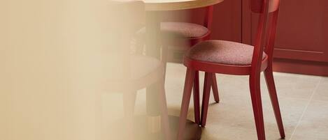 Una cocina con una mesa redonda y dos sillas rojas, armarios color beige y una ventana sobre el fregadero.