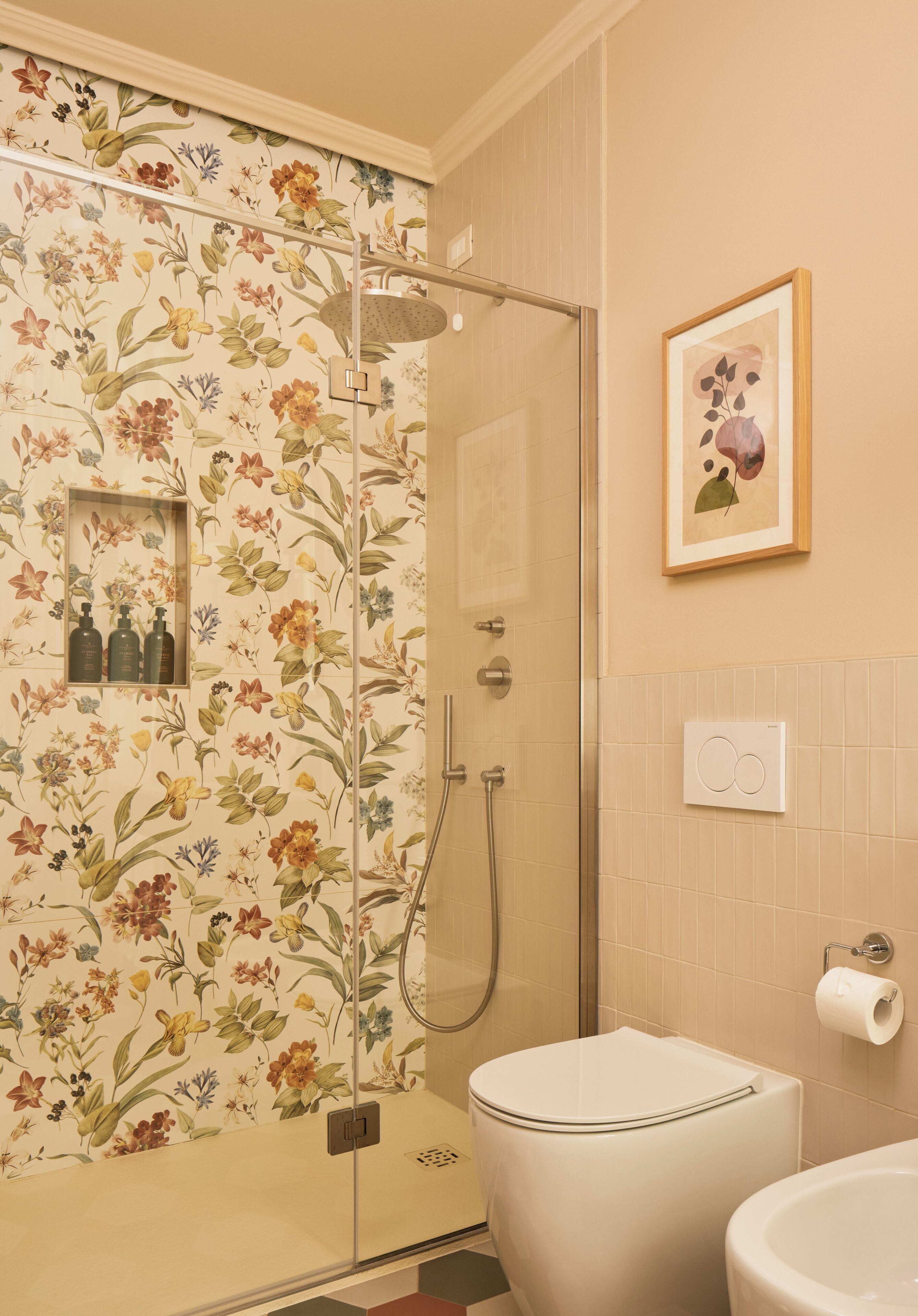 A bathroom with a shower, toilet, and a framed floral artwork on the wall.