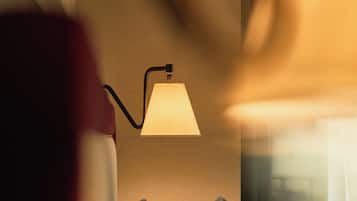 Quarto com luminária de cabeceira, janela com cortinas e cama com almofadas.