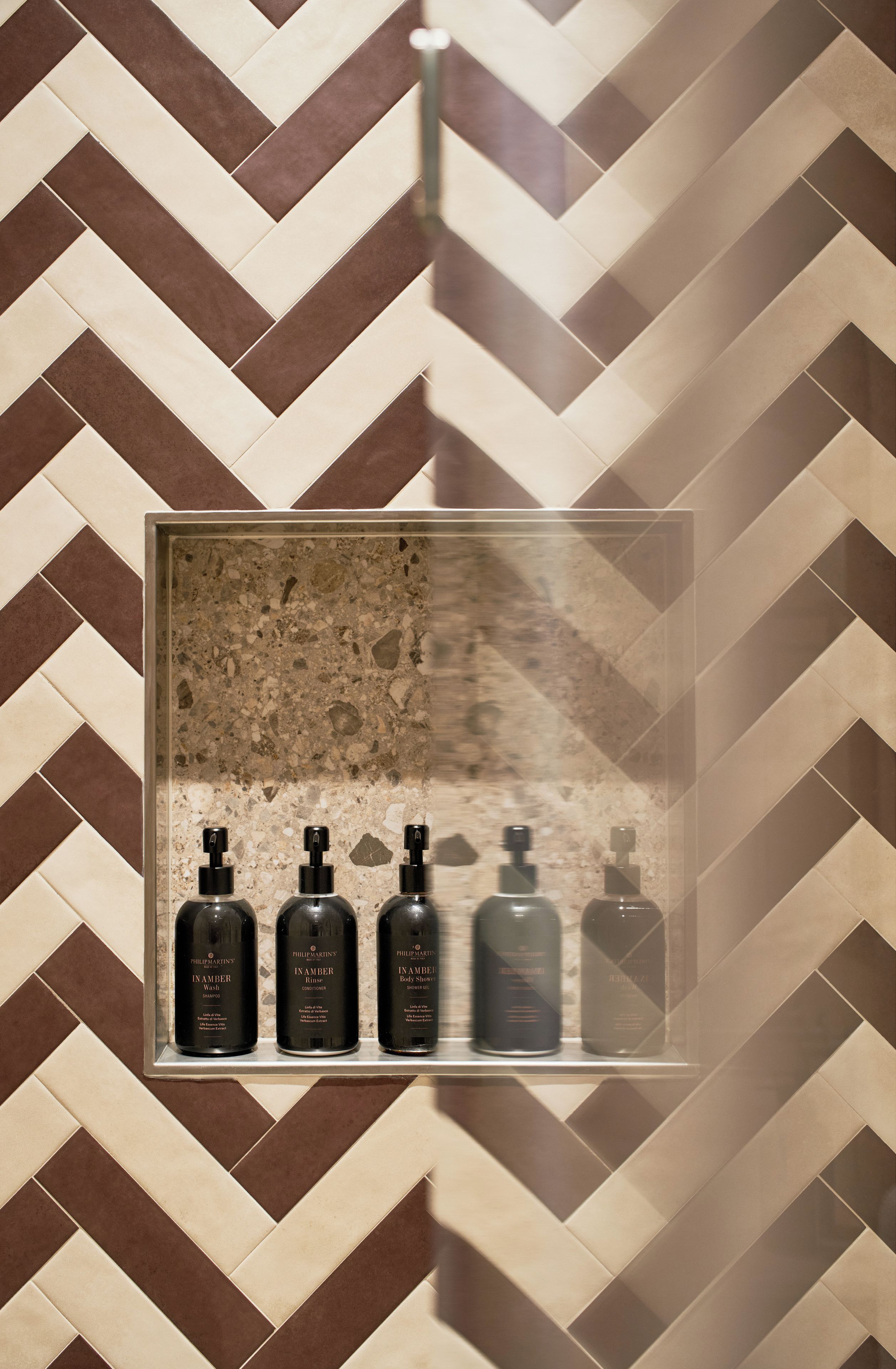 A bathroom with a herringbone tile pattern and a glass display case containing four bottles of body spray.