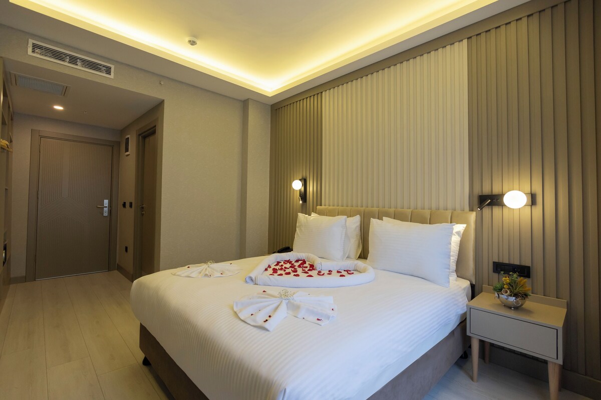 A hotel room with a large bed, a bedside table with a lamp, and a door leading to another room.