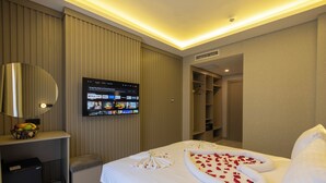 Una habitación de hotel con una cama, un televisor montado en la pared, un escritorio pequeño con un frutero y un cesto de basura.