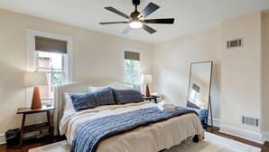 Een slaapkamer met een bed, twee nachtkastjes, een plafondventilator, een spiegel en een raam met zonwering.