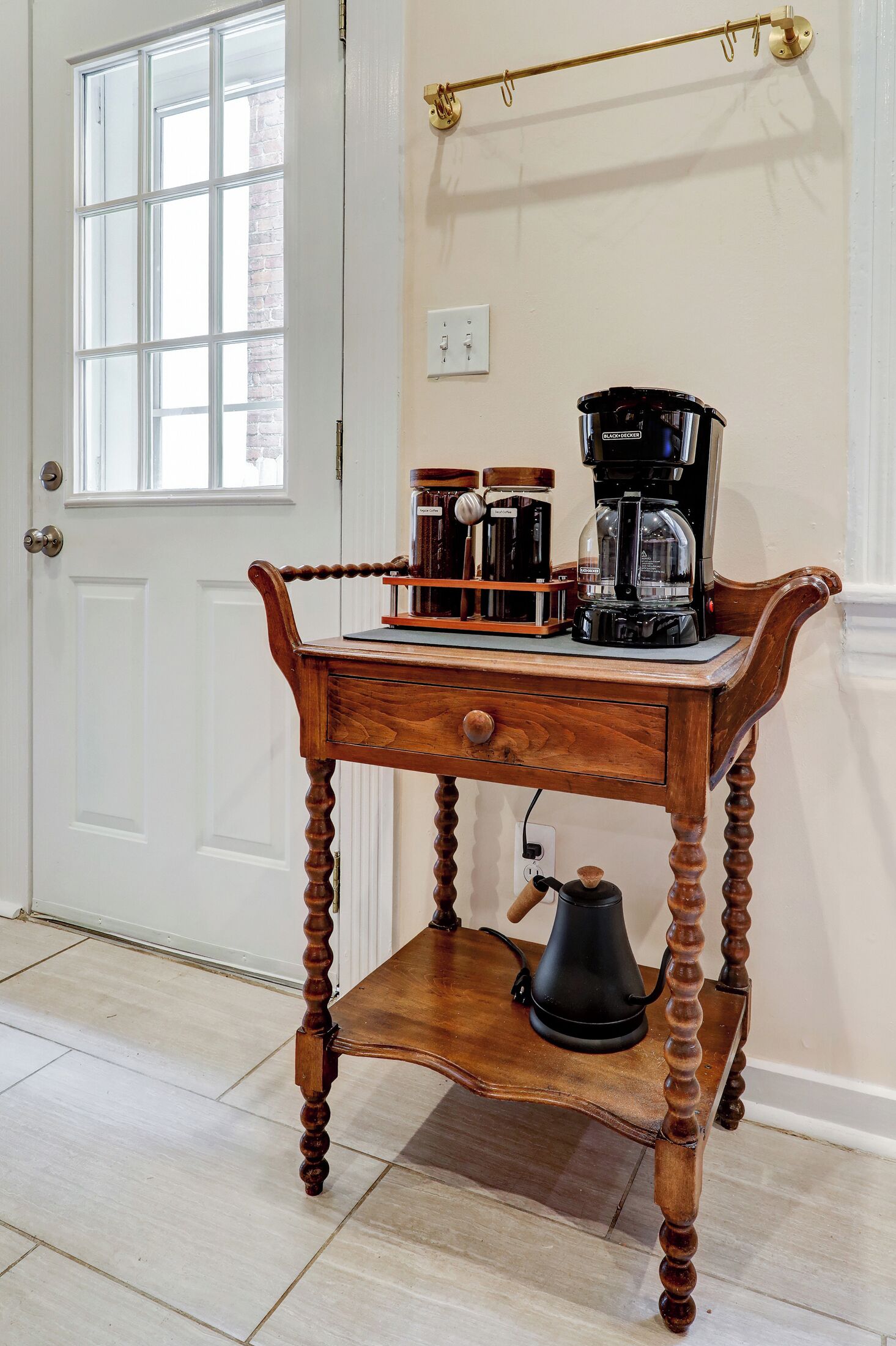 A wooden coffee table with a coffee maker and a kettle on it, placed in front of a white door with a window.