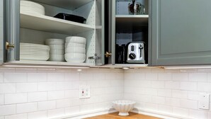 Een keuken met grijze kastjes, een houten aanrechtblad en planken met servies en een broodrooster.