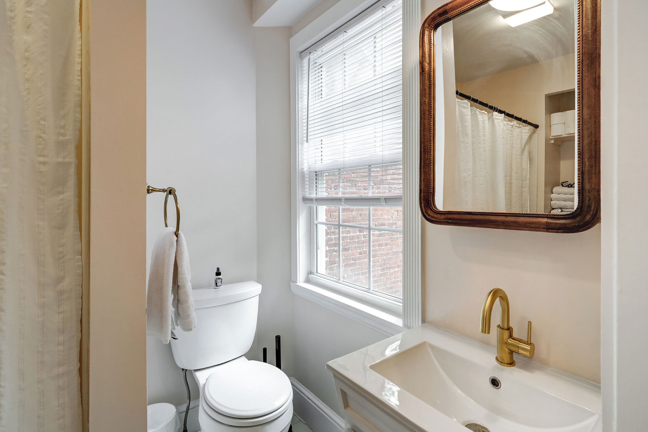 Ein Badezimmer mit Toilette, einem Waschbecken mit Goldarmatur und einem Fenster mit Jalousien.