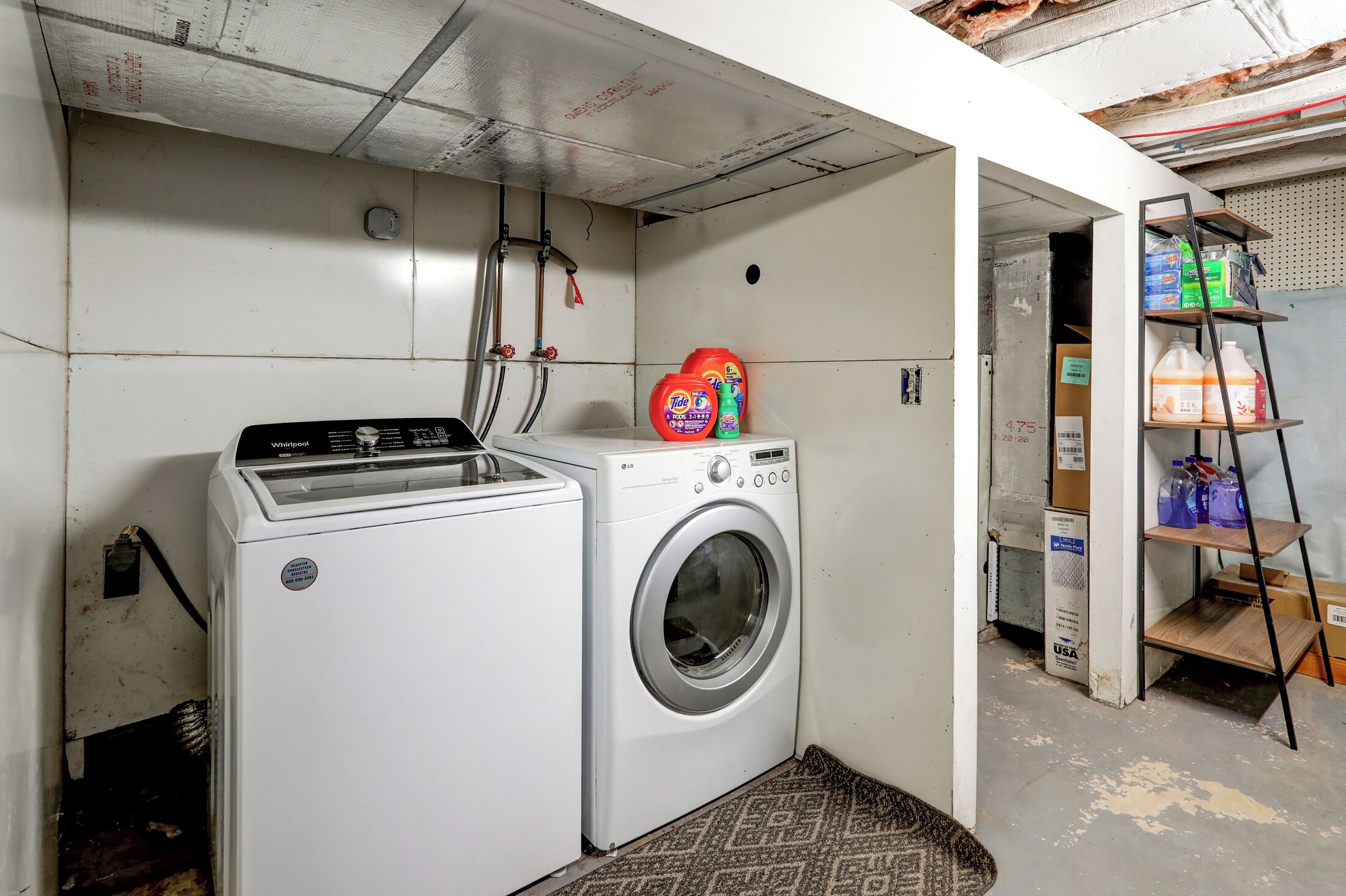 A laundry area with a Whirlpool washer and dryer, a shelf with cleaning supplies, and a ladder against the wall.