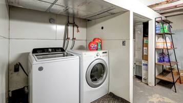A laundry area with a Whirlpool washer and dryer, a shelf with cleaning supplies, and a ladder against the wall.