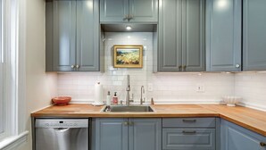 Een keuken met grijze kastjes, een roestvrijstalen vaatwasser, een houten aanrechtblad en een witte betegelde spatwand.