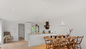 A modern kitchen with white cabinetry, a wooden dining table, and a view into the adjacent living area. - "Githe" -  from the sea by Interhome (Hals)