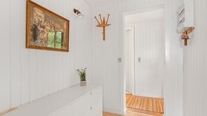 A hallway with white paneled walls, a wooden floor, a framed picture, a small plant, and a door leading to another room. - "Githe" -  from the sea by Interhome (Hals)