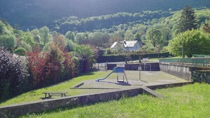 A playground with a slide and a picnic table, surrounded by lush greenery and a house in the background.