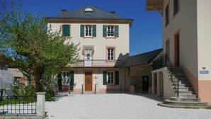 A two-story building with a balcony, a gravel courtyard, and a staircase leading to an upper floor.
