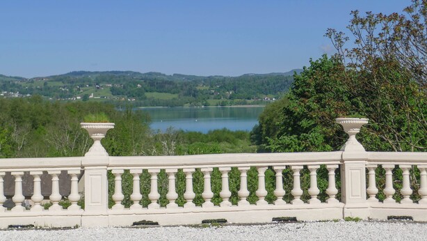 A white balustrade overlooking a lake with greenery and hills in the background.