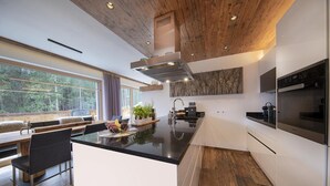 A modern kitchen with a central island, wooden ceiling, and large windows offering a view of the outdoors. - Chalet in Neukirchen Near Ski Lift (Neukirchen am Grossvenediger)