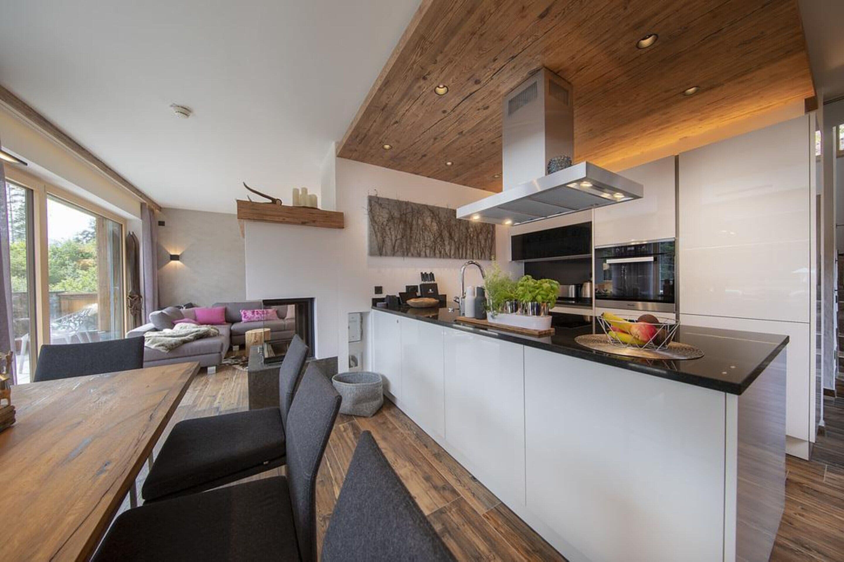 Une cuisine moderne avec un plafond en bois, des armoires blanches et un îlot central agrémenté d’un panier de fruits.