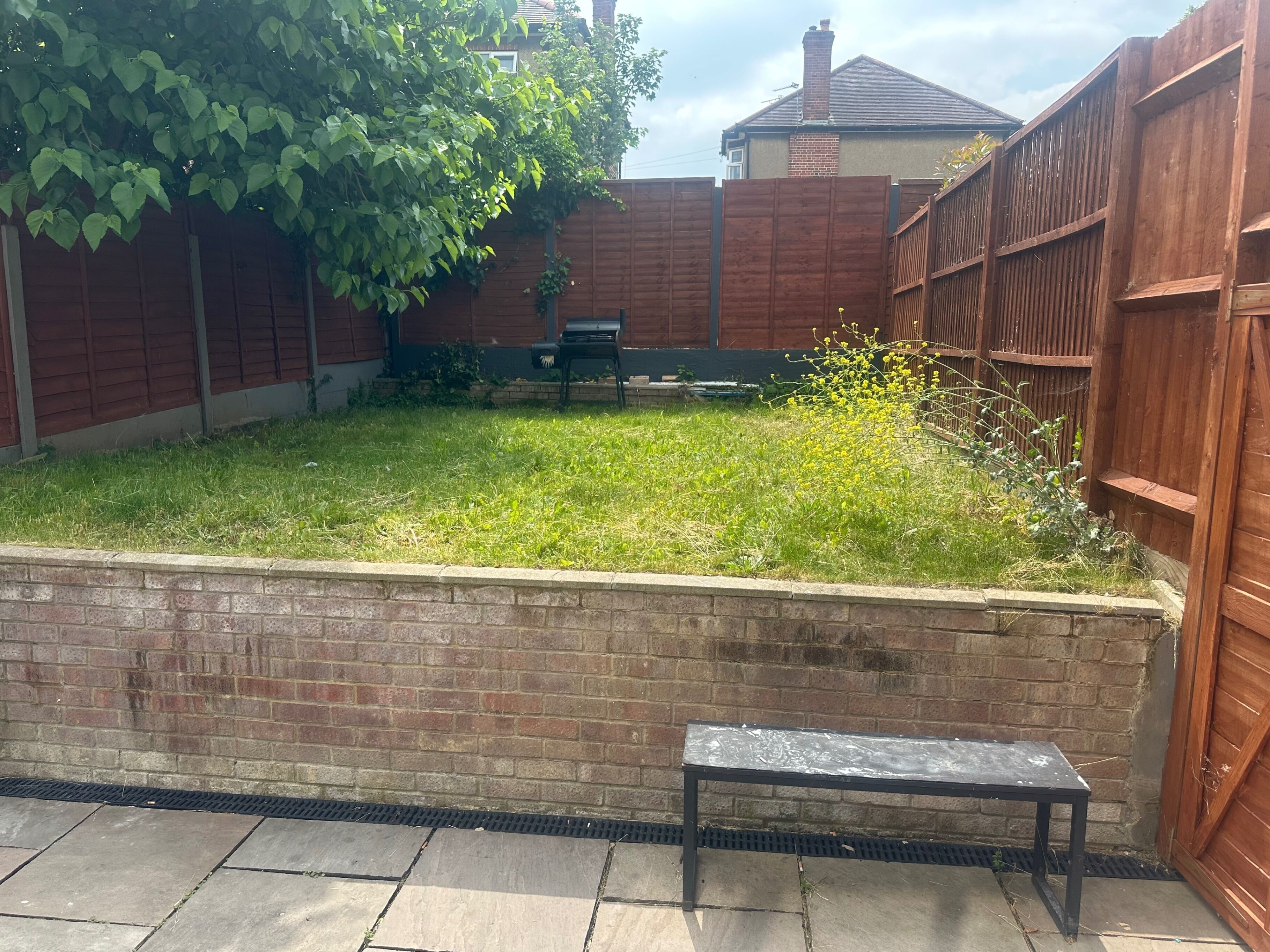 A backyard with a brick wall, a wooden fence, and a metal bench.