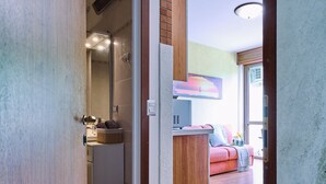 A hallway with a wooden door, a tiled floor, and a view into a living area with a sofa and a window. - Lake Maggiore - Elegant Apartment with Pool (Euroville)