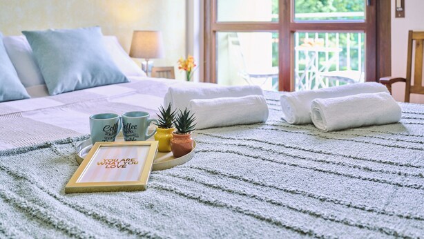 A neatly made bed with a striped blanket, two towels, two coffee mugs, a small potted plant, and a framed inspirational quote. - Lake Maggiore - Elegant Apartment with Pool (Euroville)