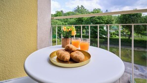 A balcony with a small table holding croissants, a potted plant, and two glasses of orange juice. - Lake Maggiore - Elegant Apartment with Pool (Euroville)