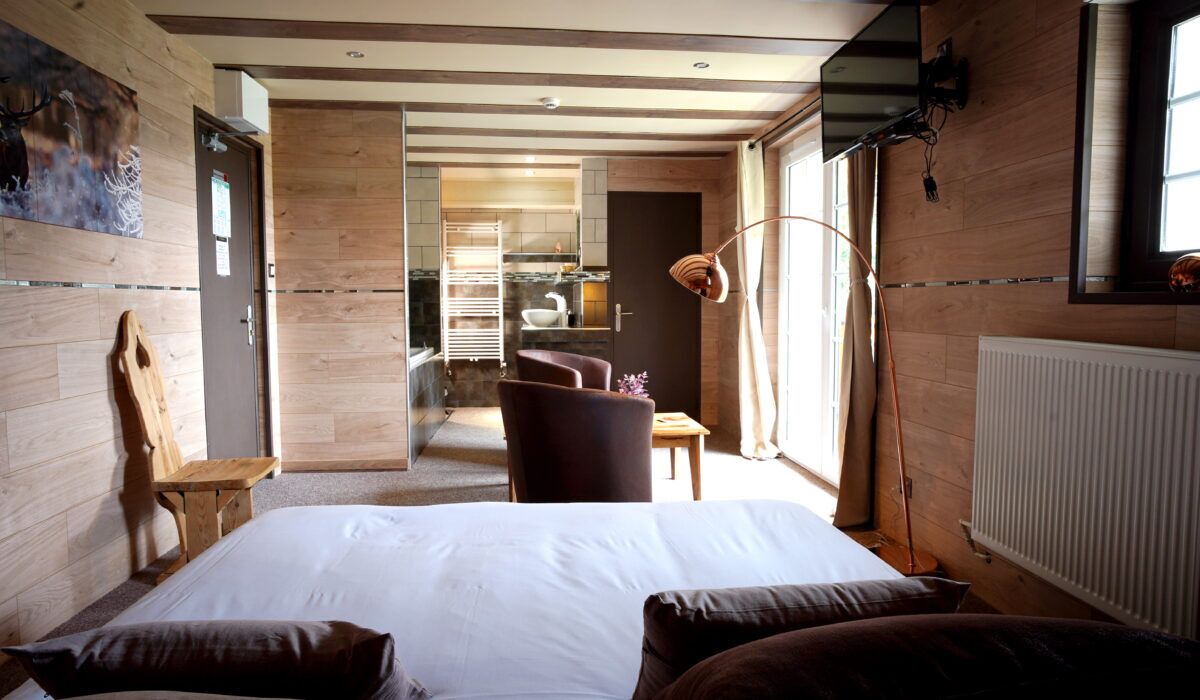 Une chambre avec un grand lit, des murs en bois, une chaise en bois, un bureau et une vue sur la salle de bain.