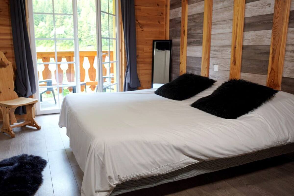 Quarto com cama, paredes de madeira, janela e varanda.