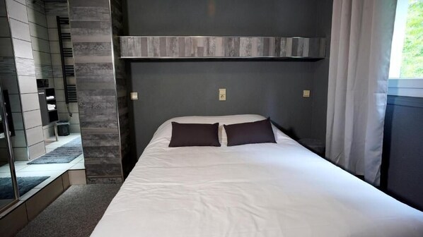 A modern hotel room with a large bed, dark headboard, and a built-in bench along the wall. - La Sapiniere (Saint-Lary-Soulan)