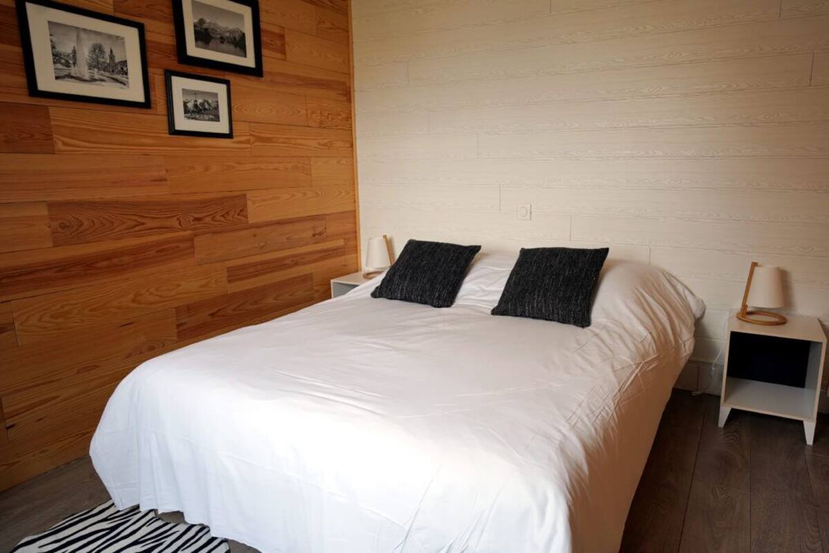 Quarto com uma cama grande, duas almofadas, cabeceira de madeira, mesa de cabeceira com abajur e três quadros na parede.