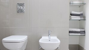 A modern bathroom with a toilet, bidet, and glass shelves with towels. - 90 sqm apartment suitable for family (Bad Soden am Taunus)