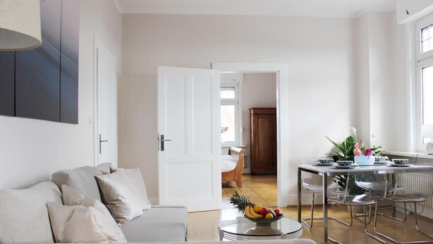 A modern living room with a sofa, a dining table with chairs, and a kitchen area in the background. - 90 sqm apartment suitable for family (Bad Soden am Taunus)