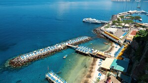 A coastal area with clear blue waters, a beach with sun loungers, and a pier with boats. - Casa Oscar - My Rental Homes (Marciano)